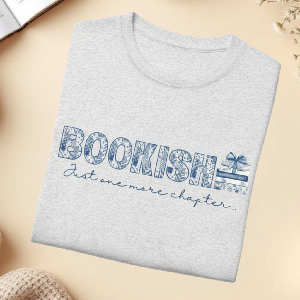 Gray tshirt with 'BOOKISH Just one more chapter' text on a beige surface with cozy elements.