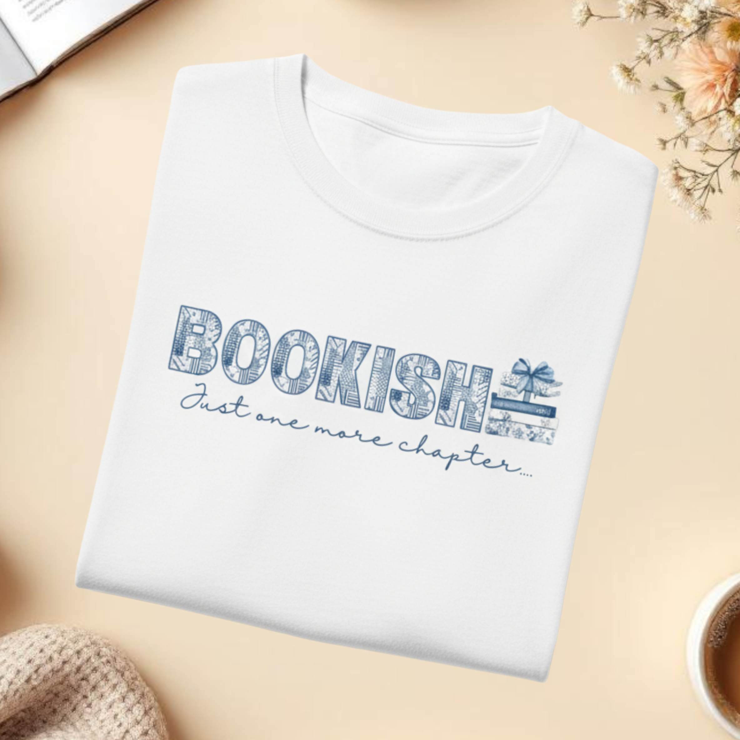 White t-shirt with 'Bookish: Just one more chapter' text on a beige surface with cozy elements.