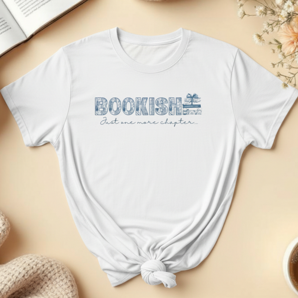 White t-shirt with 'BOOKISH Just one more chapter' text on a beige surface with books, flowers, and a cup.