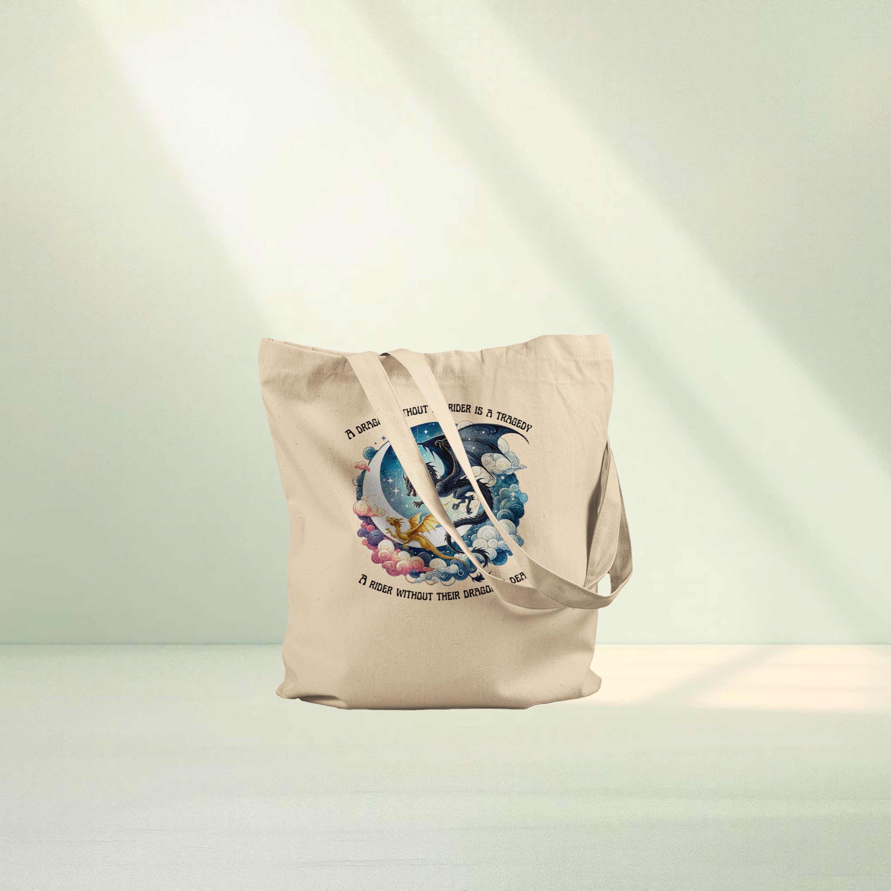 Neutral canvas tote bag featuring a circular fantasy illustration of a dragon flying alongside a rider surrounded by stylised clouds and sky tones, with romantasy themed quote text around the design.