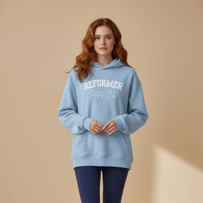 Person wearing a light blue hoodie with 'Reformer' text and dark blue leggings on a beige background